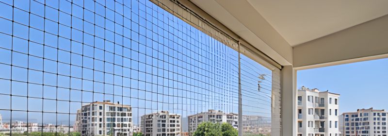 Apartman balkonunun korkuluktan tavana kadar siyah ince fileyle kapatıldığı, dışarıda yeni konutların göründüğü balkon