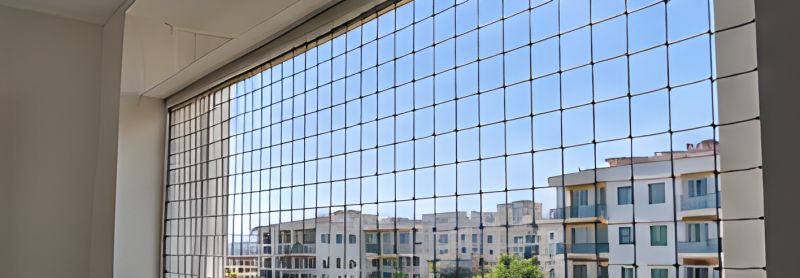 Geniş pencerenin önüne gerilmiş güvenlik filesi ve arkasında apartmanlar